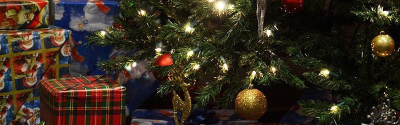 photo of base of christmas tree, with white lights on it and wrapped boxes sitting to the left.